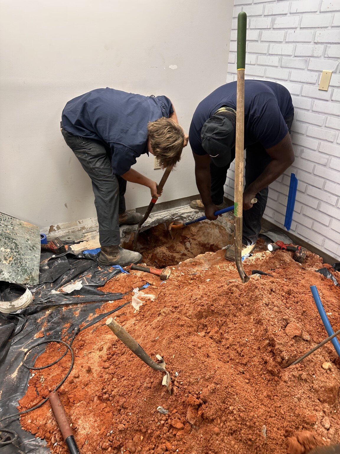 Two Quick Rooter plumbers working in an indoor excavation
